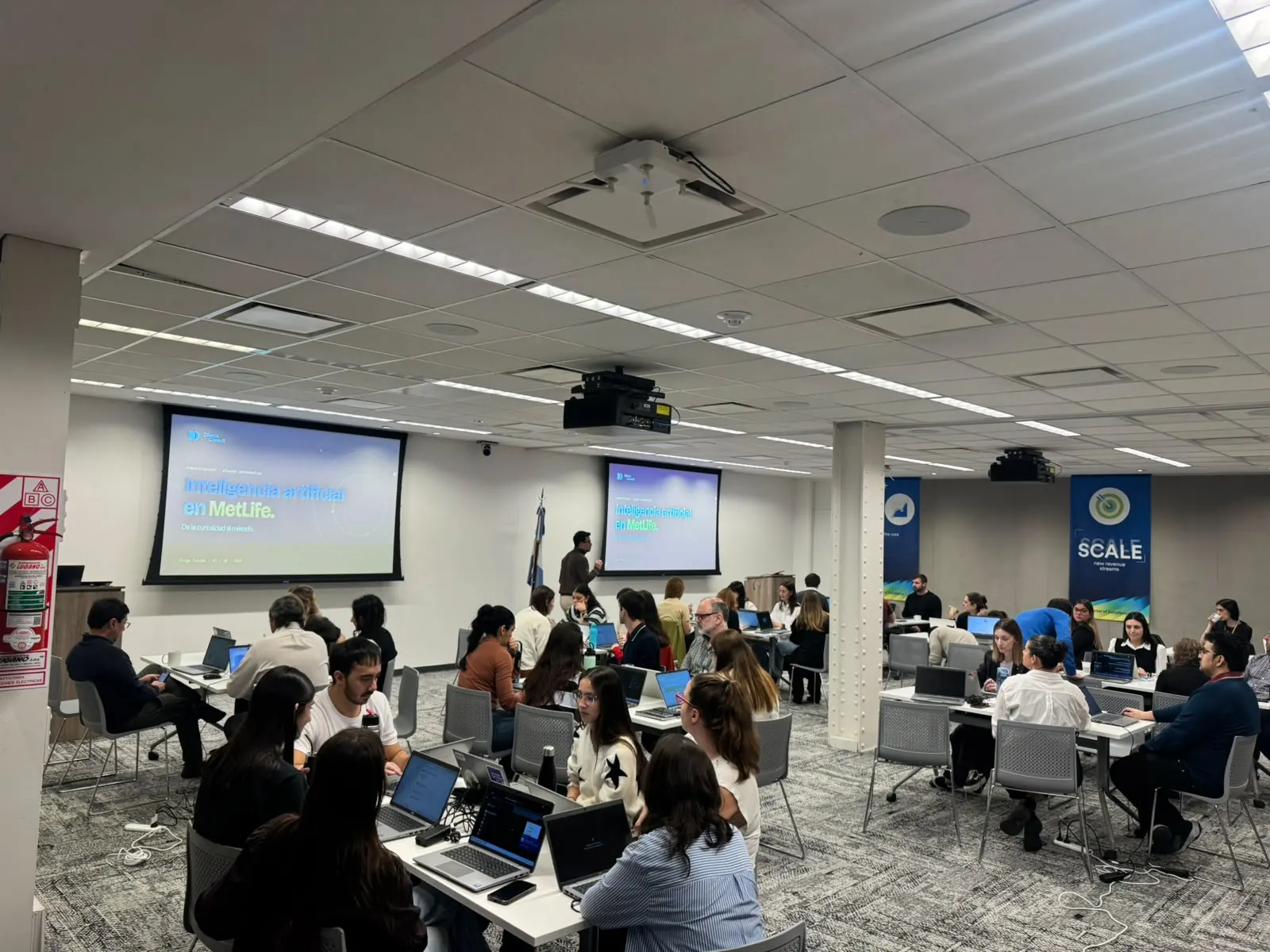 Participantes de MetLife Argentina con notebooks durante un workshop de Claude Enterprise, con la presentación «Inteligencia artificial en MetLife» en dos pantallas, octubre de 2026